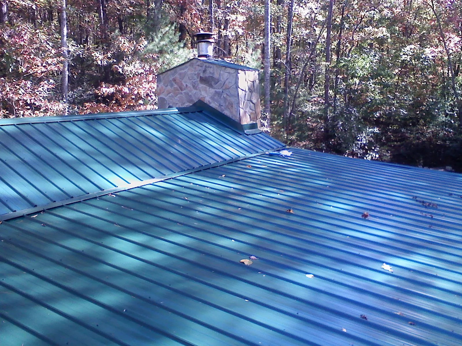 New green metal roof and stone chimney surrounded by autumn woods in Mulberry